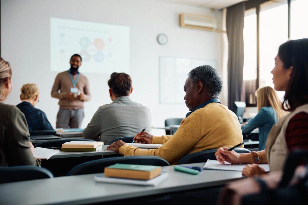 Black senior student man writing while attending adult education class in lecture hall.