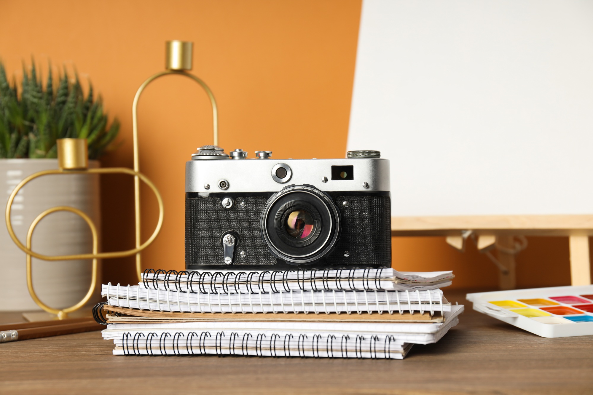 Vintage camera, paints and notepads on table on orange background
